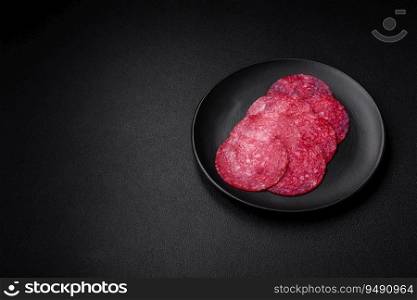Delicious smoked salami sausage with salt, spices and herbs cut into slices on a dark concrete background