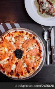 Delicious smoked Salmon thin crispy italian pizza with premium black Caviar close up top view shot