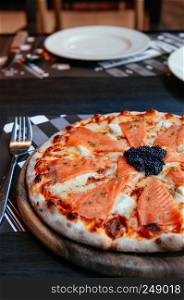 Delicious smoked Salmon thin crispy italian pizza with premium black Caviar close up shot