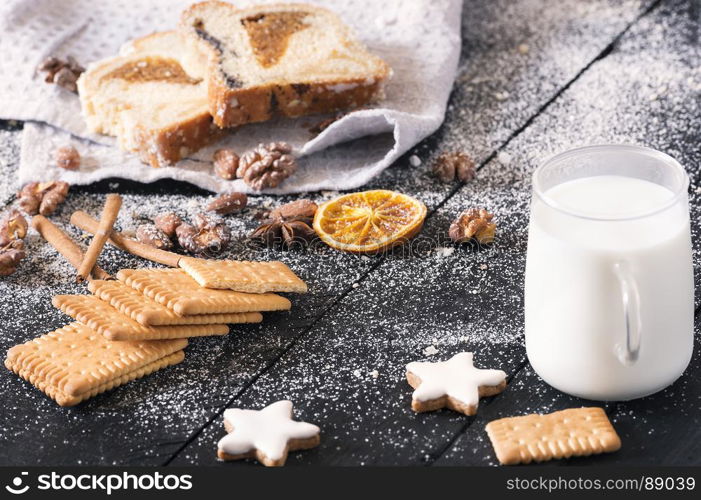 Delicious snack with plain biscuits, star shaped cookies, roasted nuts, sponge cake, all covered with powder sugar, and a cup of milk on a vintage table.