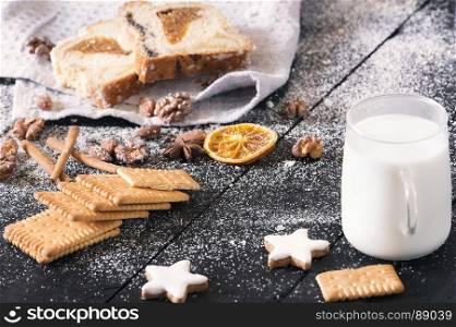 Delicious snack with plain biscuits, star shaped cookies, roasted nuts, sponge cake, all covered with powder sugar, and a cup of milk on a vintage table.