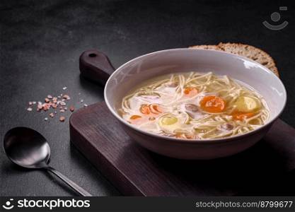 Delicious soup with noodles, chicken and carrots with spices and herbs on a dark concrete background