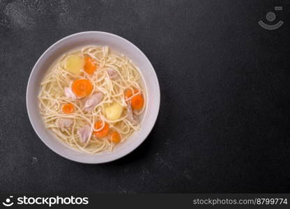 Delicious soup with noodles, chicken and carrots with spices and herbs on a dark concrete background