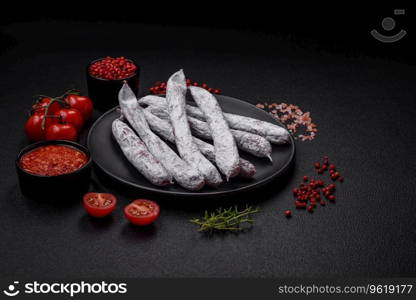 Delicious Spanish smoked sausage fuet with salt and spices on a dark concrete background