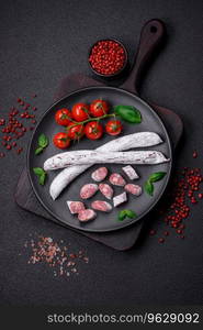 Delicious Spanish smoked sausage fuet with salt and spices on a dark concrete background