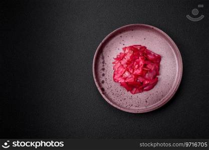 Delicious spicy pink cabbage sliced and cooked in Korean style on a ceramic plate on a dark concrete background