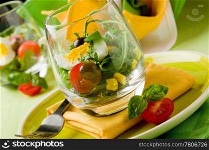 Delicious starter of mixed salad inside a glass on green wooden table