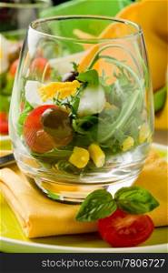 Delicious starter of mixed salad inside a glass on green wooden table