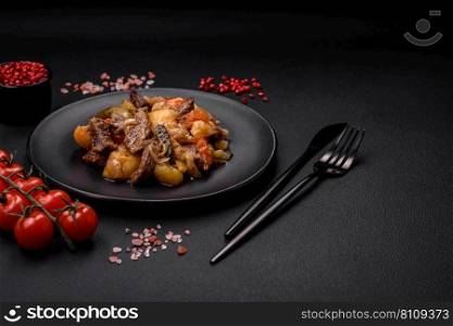Delicious stew with potatoes, tomatoes, beef, onions and carrots on a ceramic plate on a dark concrete background