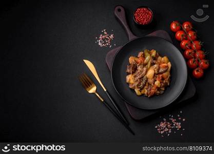Delicious stew with potatoes, tomatoes, beef, onions and carrots on a ceramic plate on a dark concrete background