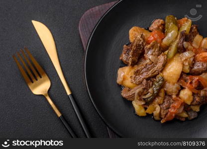 Delicious stew with potatoes, tomatoes, beef, onions and carrots on a ceramic plate on a dark concrete background