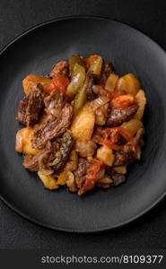 Delicious stew with potatoes, tomatoes, beef, onions and carrots on a ceramic plate on a dark concrete background