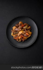 Delicious stew with potatoes, tomatoes, beef, onions and carrots on a ceramic plate on a dark concrete background