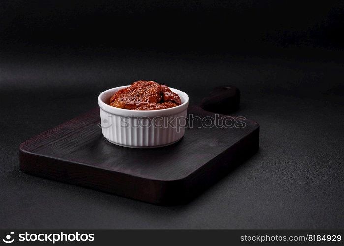 Delicious sun dried tomatoes in oil in a white ceramic bowl on a dark concrete background