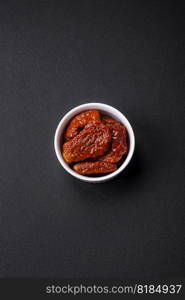 Delicious sun dried tomatoes in oil in a white ceramic bowl on a dark concrete background