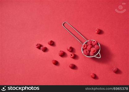 Delicious sweet berries in a colanderon on paper background with place for text. Flat lay. Concept of vegetarian food.. Freshly picked sweet raspberry on a red paper background. Colorful organic berries pattern.