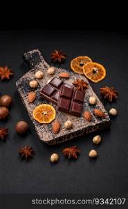Delicious sweet black chocolate broken into cubes on a wooden cutting board on a dark concrete background