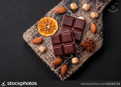 Delicious sweet black chocolate broken into cubes on a wooden cutting board on a dark concrete background