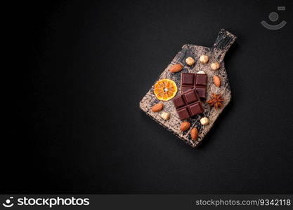 Delicious sweet black chocolate broken into cubes on a wooden cutting board on a dark concrete background
