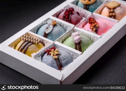 Delicious sweet colorful mochi desserts or ice cream with rice dough and toppings in a cardboard box on a dark concrete background