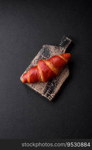 Delicious sweet crunchy red croissant with cream filling on dark textured concrete background