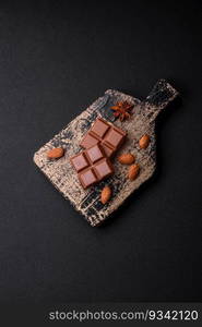 Delicious sweet milk chocolate broken into cubes on a wooden cutting board on a dark concrete background