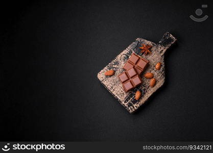 Delicious sweet milk chocolate broken into cubes on a wooden cutting board on a dark concrete background