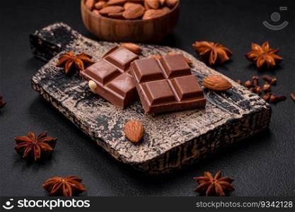 Delicious sweet milk chocolate broken into cubes on a wooden cutting board on a dark concrete background