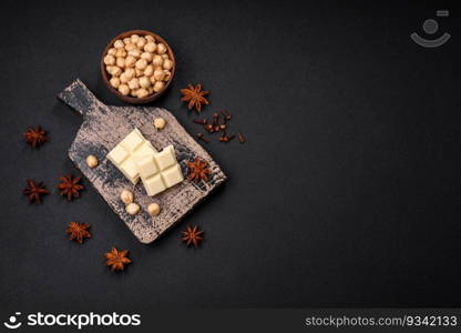 Delicious sweet white chocolate broken into cubes on a wooden cutting board on a dark concrete background