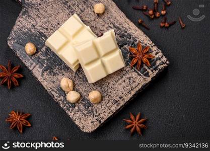 Delicious sweet white chocolate broken into cubes on a wooden cutting board on a dark concrete background
