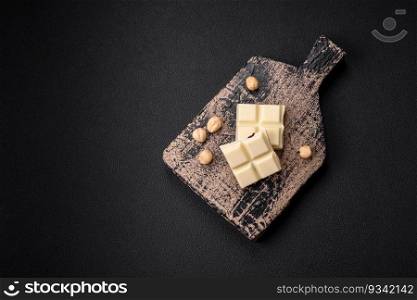 Delicious sweet white chocolate broken into cubes on a wooden cutting board on a dark concrete background