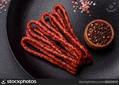 Delicious thin smoked meat sausages with spices and herbs on a dark concrete background