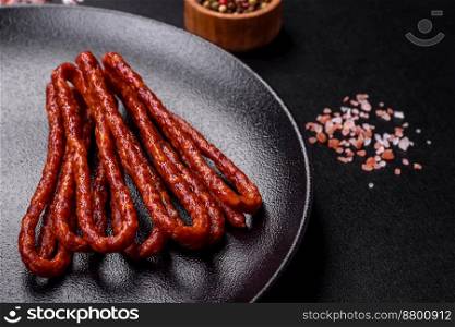 Delicious thin smoked meat sausages with spices and herbs on a dark concrete background
