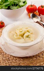 delicious tortellini pasta in broth with vegetables on white table