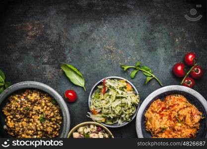 Delicious various vegetarian salads in bowls on dark rustic background, top view, border. Healthy eating, Vegetarian or vegan food concept