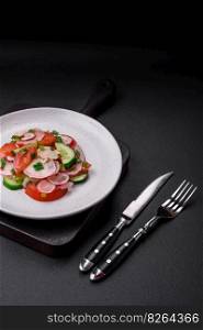 Delicious vegan salad of fresh vegetables of tomatoes, cucumbers and radishes with salt and spices on a dark concrete background