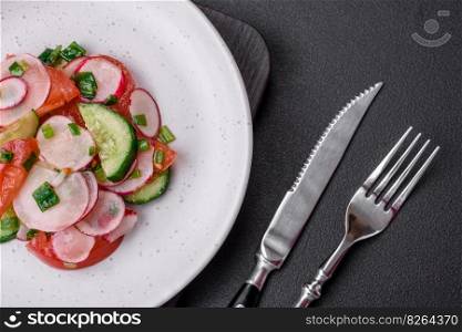 Delicious vegan salad of fresh vegetables of tomatoes, cucumbers and radishes with salt and spices on a dark concrete background