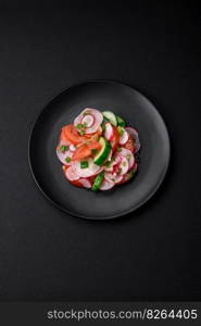 Delicious vegan salad of fresh vegetables of tomatoes, cucumbers and radishes with salt and spices on a dark concrete background