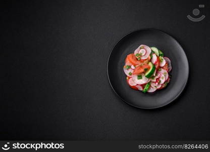 Delicious vegan salad of fresh vegetables of tomatoes, cucumbers and radishes with salt and spices on a dark concrete background