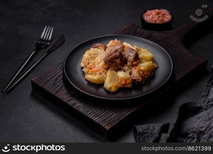 Delicious vegetable stew with beef, potatoes, carrots and cabbage in a black plate against a dark concrete background. Delicious vegetable stew with beef, potatoes, carrots and cabbage in a black plate