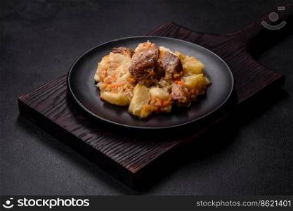 Delicious vegetable stew with beef, potatoes, carrots and cabbage in a black plate against a dark concrete background. Delicious vegetable stew with beef, potatoes, carrots and cabbage in a black plate