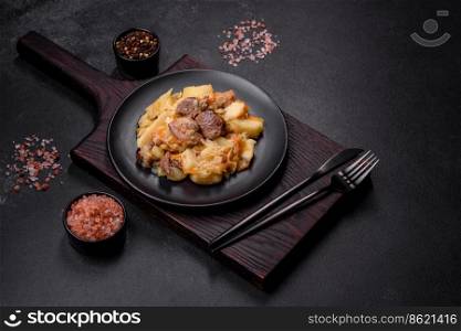 Delicious vegetable stew with beef, potatoes, carrots and cabbage in a black plate against a dark concrete background. Delicious vegetable stew with beef, potatoes, carrots and cabbage in a black plate