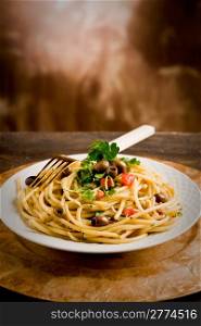 delicious vegetarian dish of pasta with olives and parsley on wooden table