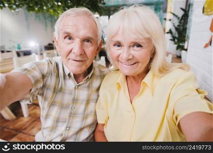 delighted senior couple hugging sitting cafe shooting selfie