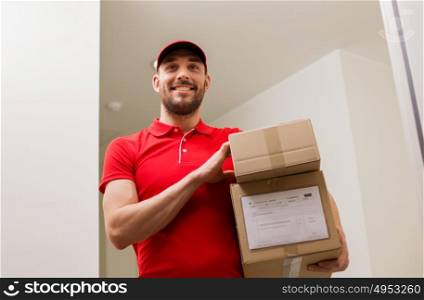delivery, mail, people and shipment concept - happy man in red uniform with parcel boxes in corridor at open customer door. delivery man with parcel boxes at customer door