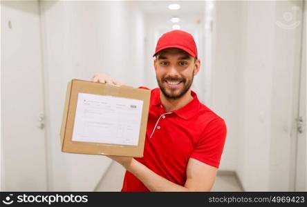 delivery, mail, people and shipment concept - happy man in red uniform with parcel box in corridor. delivery man with parcel box in corridor