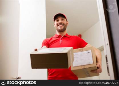 delivery, mail, people and shipment concept - happy man in red uniform with parcel boxes at open customer door. delivery man with parcel boxes at customer door