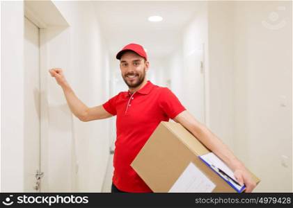 delivery, mail, people and shipment concept - happy man in red uniform with parcel box in corridor knocking on door. delivery man with parcel box knocking on door