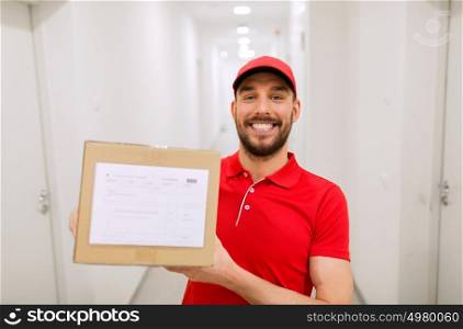delivery, mail, people and shipment concept - happy man in red uniform with parcel box in corridor. delivery man with parcel box in corridor