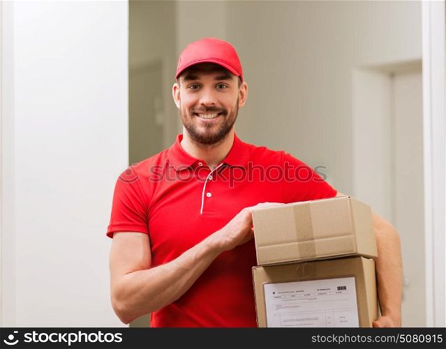delivery, mail, people and shipment concept - happy man in red uniform with parcel boxes in corridor. delivery man with parcel boxes in corridor